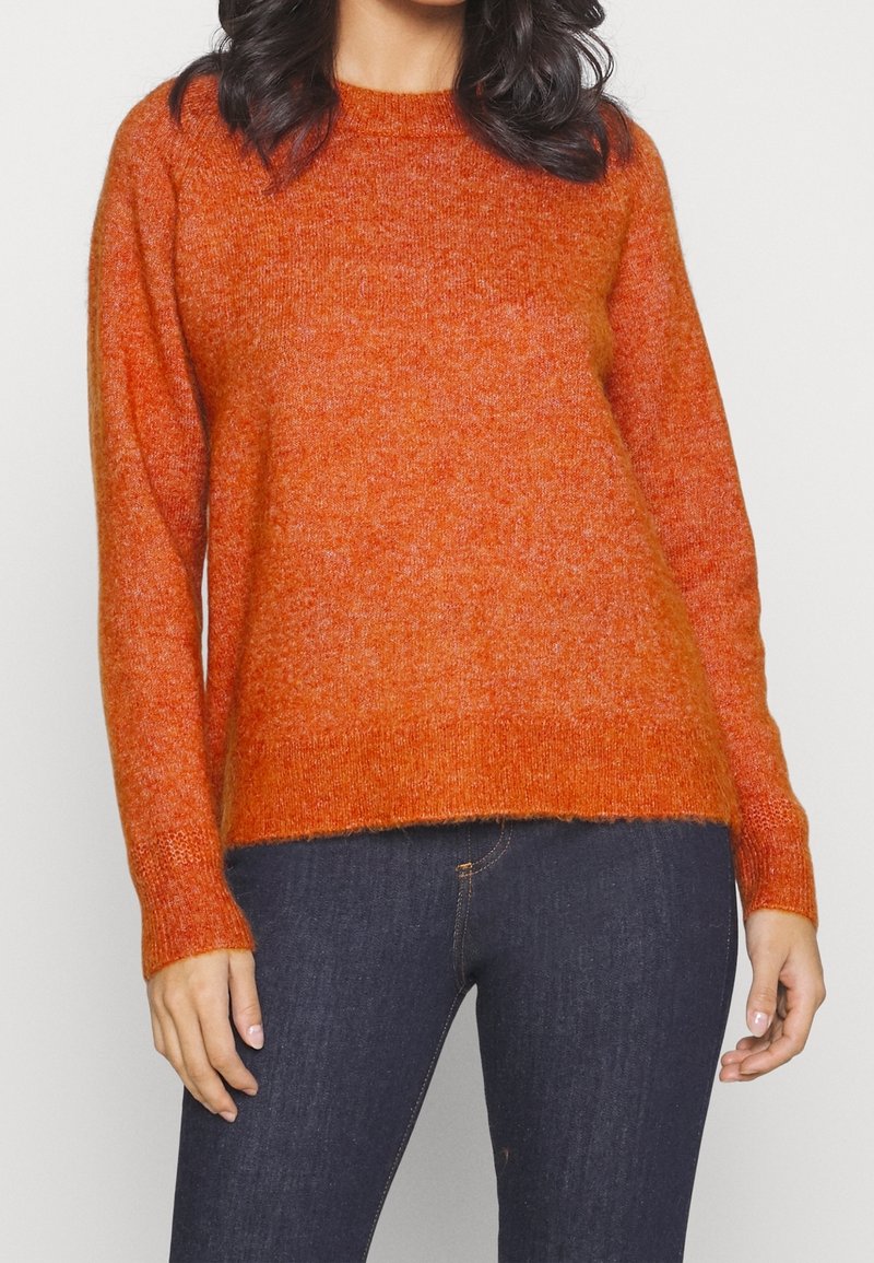 Pomarańczowy sweter z dzianiny z okrągłym dekoltem, długimi rękawami i luźnym krojem. Miękka faktura i prążkowany dół dodają wizualnego zainteresowania.