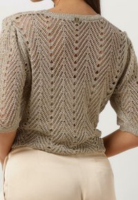 Blouse en maille argentée avec un motif en chevrons, manches courtes et détails en tissage ouvert ; dotée d'un col rond et d'un accent de bouton dans le dos.