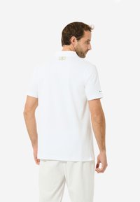 Weißes Polohemd mit kurzen Ärmeln und Kragen, mit einem Logotag auf der Rückseite und einem kleinen Akzentdetail am Ärmel. Glatter Stoffeindruck.