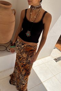 Top nero abbinato a una lunga gonna con stampa animale, caratterizzata da strisce arancioni e nere. Gli accessori includono collane a strati e bracciali.
