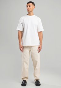 White cotton t-shirt with short sleeves, paired with beige wide-leg pants and black shoes. Simple design, relaxed fit, minimal accents.