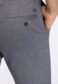 Grau maßgeschneiderte Hose mit einem dezenten Hahnentrittmuster, die über eine Seitentasche, eine Knopfverzierung und einen strukturierten Stoff verfügt.