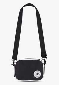 Borsa a tracolla nera in tela con accenti bianchi, forma rettangolare, tracolla regolabile, chiusura con zip e una toppa circolare con logo.