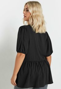 Blusa nera a maniche corte con maniche a sbuffo e vita arricciata. Tessuto morbido con design a peplo, modellata per una vestibilità rilassata.