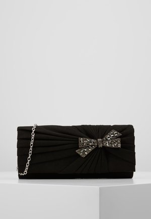 Schwarze rechteckige Clutch mit gerafftem Stoff, verziert mit einer dunklen Strasssteinschleife und silberner Kettenriemen, auf einem weißen Sockel.