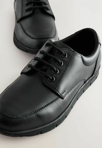 Chaussures en cuir noir avec une surface lisse, un bout rond et six œillets pour les lacets. Semelle en caoutchouc légèrement texturée pour une meilleure adhérence.