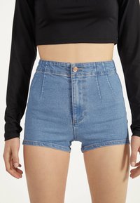 Höga denimshorts i ljusblått med dragkedja och knäppning, med framfickor och en slät, något sliten textur.