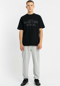 Czarny bawełniany t-shirt z nadrukiem "RUSTED SOUL" w kolorze szarym; w zestawie z jasnoszarymi spodniami dresowymi. Obuwie czarne z białymi i brązowymi akcentami.