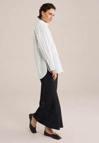 White striped button-up shirt, long black skirt, and dark flat shoes. The shirt has a high collar and slightly oversized fit.