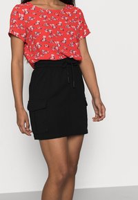 Červený květinový vzorovaný top s krátkým rukávem v kombinaci s černou bavlněnou sukní s elastickým pasem a cargo kapsami.