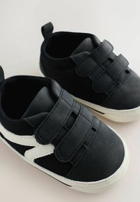 Black fabric sneakers with white accents, featuring Velcro straps and textured rubber soles, designed for ease of wear and comfort.