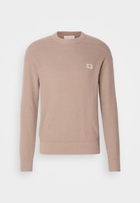 Pull en maille beige à col rond avec manches longues et petit patch logo "CK" sur la poitrine gauche, avec poignets et ourlet côtelés.