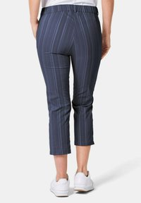 Marineblauwe, cropped broek met verticale strepen, elastische tailleband en zijzakken. Draagt met witte sneakers. Glad stof textuur.