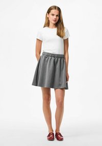 Gonna a corolla grigia con vita elastica abbinata a una t-shirt bianca aderente. La modella indossa scarpe borgogna con design a strap.