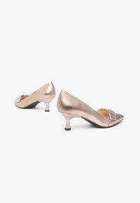 Talons aiguilles à bout pointu en or rose métallisé. Comprend une petite boucle décorative et un talon stiletto de hauteur intermédiaire, avec une finition satin lisse.