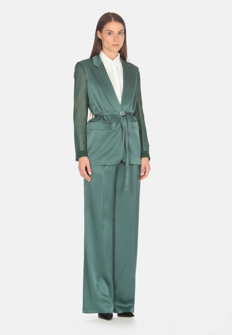 Set din satin teal, cu un curea cu cataramă rotundă, două buzunare frontale și mâneci din material transparent contrastant. Asortat cu o cămașă albă cu guler.