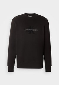 Czarna bluza z bawełnianego materiału, z okrągłym dekoltem i ściągaczami przy rękawach. Z przodu znajduje się haftowane logo "Calvin Klein Jeans".
