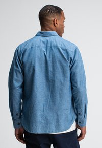 Lichtblauwe, lange mouwen shirt van een gestructureerde stof, met een button-down kraag en manchetrokken mouwen. Voorzien van een rechte zoom en een logo detail nabij de zoom.