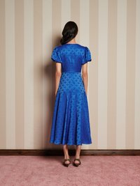 Vestido azul até ao joelho com mangas bufantes e padrão floral texturizado. Material semelhante a cetim com corpete justo e saia rodada.