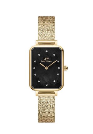 Kuldne ristkülikukujuline kell musta näo, kaunistatud tunni markeritega ja tekstureeritud kuldse võrgu rihmaga. Omab kaubamärgi logo "Daniel Wellington."