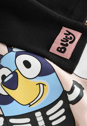 Svart ribbat tyg med en rosa etikett märkt "Bluey." Har en färgglad tecknad karaktär i blå och gula nyanser, mot en ljusrosa bakgrund.