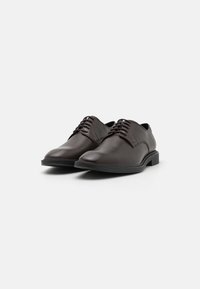 Chaussures habillées en cuir marron avec une finition lisse, dotées d'un bout arrondi, d'un système de laçage et d'une semelle plate en caoutchouc noir.