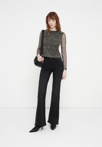 Black flared jeans paired with a long-sleeve sheer top featuring a tiger stripe pattern in black and gold. Includes a small black bag.