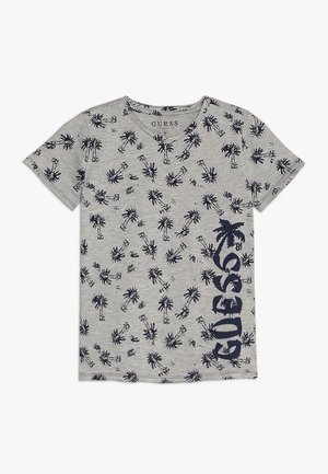 T-shirt gris à manches courtes avec motif de palmier noir et grand logo vertical "GUESS" sur le côté droit.
