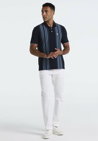Marineblauw poloshirt met verticale strepen in lichtblauw en wit, korte mouwen en een kraag. Gekocht met witte broeken en sneakers.