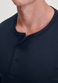 Donkerblauw katoenen henley shirt met een ronde halslijn, drie knopen aan de placket en korte mouwen. Vlotte textuur met subtiele stitching.
