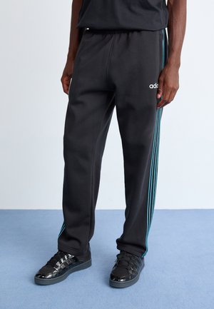 Sorte sportsbukser med elastisk talje, prydet med blå striber ned langs siderne; båret med sorte sneakers, der har glansfulde detaljer.