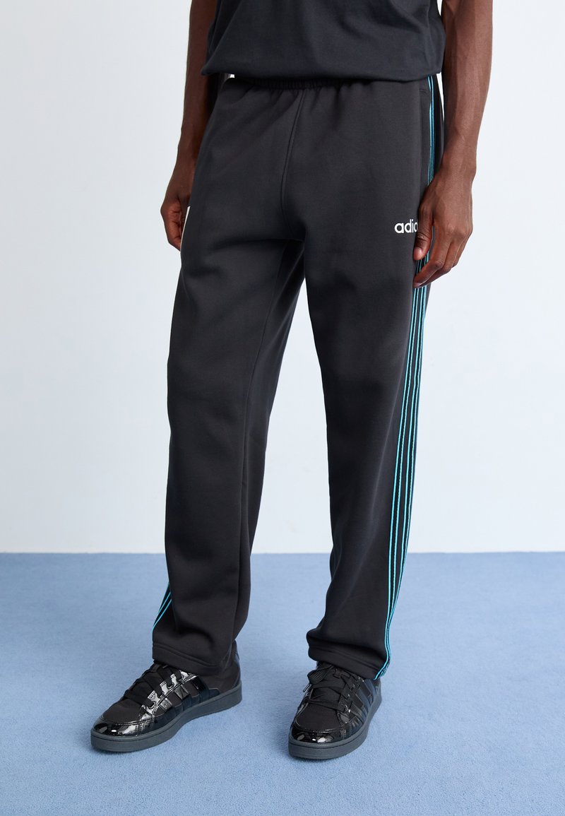 Svarte treningbukser med elastisk midje, med blå striper nedover sidene; brukt med svarte joggesko med blanke detaljer.