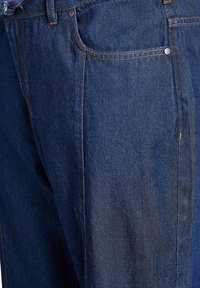 Tumši zili džinsi ar gludu tekstūru, kontrastējošām šuvēm un piecu kabatu dizainu, ar sudraba pogu un kniedēm.