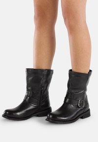 Stivaletti neri in pelle con punta rotonda, zip laterale e una fascia con fibbia. Texture morbida e tacco basso e squadrato.