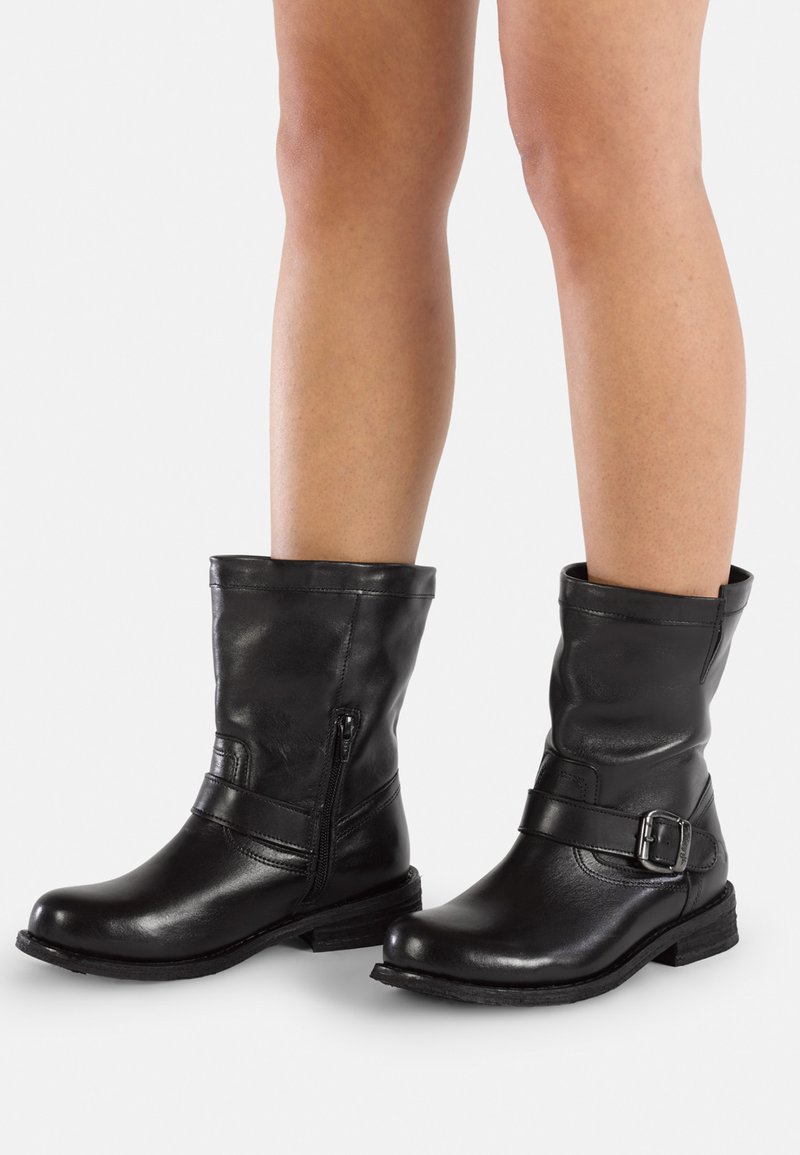 Stivaletti neri in pelle con punta rotonda, zip laterale e una fascia con fibbia. Texture morbida e tacco basso e squadrato.