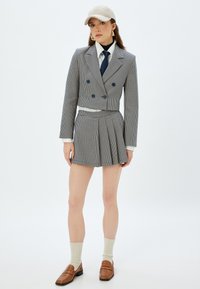 Geverifieerde pakset met een cropped blazer met dubbelgeknoopte knopen, een geplooide rok, gecombineerd met een pet en bruine loafers.