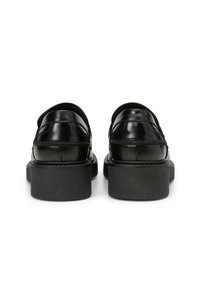 Mocassins en cuir verni noir avec un bout arrondi et de semelles en caoutchouc noir épaisses et basses. Détails de couture le long du talon et de la tige.