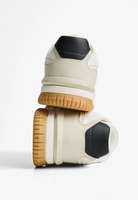 Bežové tenisky s textúrovaným povrchom, s čiernym koženým akcentom na päte a gumovou podrážkou s vzorovanými drážkami.