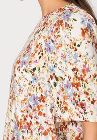 Blommig topp med vit bakgrund och flerfärgade blommönster, korta ärmar och en avslappnad passform.