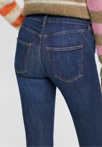 Vaqueros de mezclilla azul oscuro con un diseño ajustado, que cuentan con dos bolsillos traseros y detalles de costura clara. La tela tiene una textura suave.