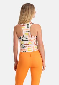 Canottiera sportiva con motivi colorati di montagne e natura, realizzata in tessuto leggero. Abbinata a leggings a vita alta di un vivace arancione.