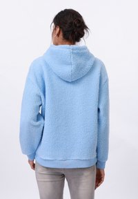Felpa con cappuccio blu chiaro in pile, con una superficie morbida e texture, che presenta un cappuccio, polsini e bordo inferiore a costine. Vestibilità rilassata, design di lunghezza media.