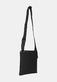 Borsa a tracolla nera con spallaccio regolabile, realizzata in tessuto testurizzato. Presenta una chiusura con zip e una forma rettangolare slanciata. Design minimalista.