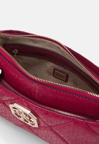 Červená prošívaná kabelka s lesklým povrchem. Zlaté kovové doplňky a detail na zipu. Vnitřek má béžovou podšívku s označením značky.