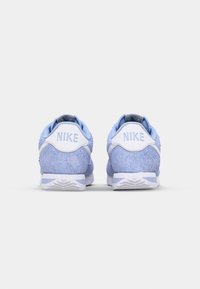 Zili zamaka sporta apavi ar baltām akcentu detaļām, kas aprīkoti ar fakturētu virspusi, kontrastējošu papēdi ar "NIKE" zīmolu un rakstainu zoli.
