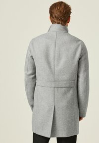 Cappotto in lana grigia con motivo a spina di pesce, colletto strutturato e dettaglio della cintura in vita. Silhouette aderente con schiena ventilata.