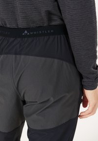 Mustat ja harmaat urheiluhousut, joissa on tekstuurilla varustettu vyötärönauha ja "WHISTLER"-logo. Housut on suunniteltu vaihtelevilla kangas tekstuureilla ja paneeleilla.