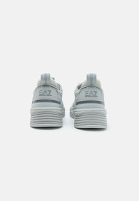 Gray sneakers with a textured upper, featuring a rounded heel and a pronounced tread. Notable branding on the back adds detail.