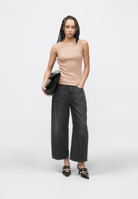 Beiger ärmelloser Oberteil, dunkelblaue Jeans mit weitem Bein, schwarze Schuhe mit Absatz und Schnallen sowie eine schwarze Clutch. Einfaches, modernes Design und neutrale Farben.