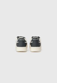 Svarte sneakers med kremfargede detaljer, laget av glatt syntetisk materiale, flat såle og med en logo på baksiden. Minimalistisk design, lavtoppsstil.